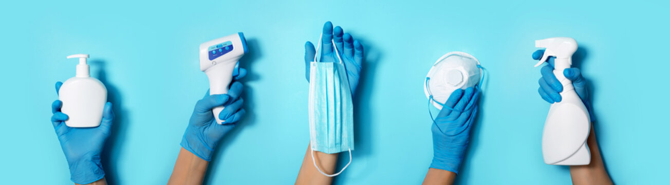 Raised hands in medical gloves holding masks, sanitizers, soap, non contact thermometer on blue background. Banner. Copy space. Health protection equipment during quarantine Coronavirus pandemic