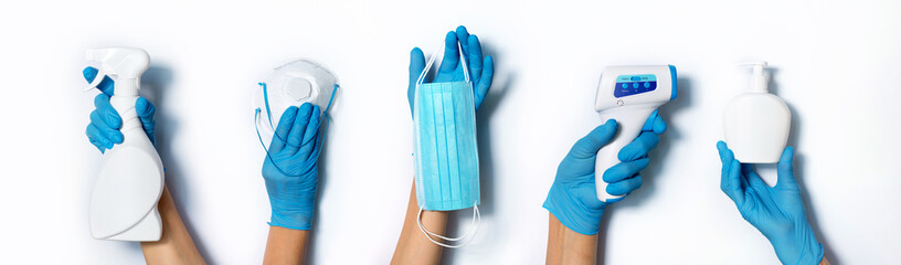 Raised hands in medical gloves holding masks, sanitizers, soap, non contact thermometer on white...
