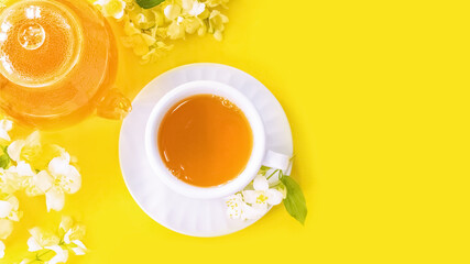 flower tea in a cup and teapot on a yellow background and Jasmine flowers top view. background with green hot tea in a cup and teapot and Jasmine flowers.
