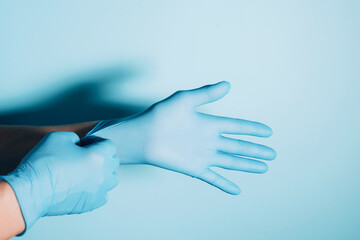 Woman doctor wears medical gloves over blue background. Copy space. National Doctors' Day. International Nurses Day. Health protection equipment during quarantine Coronavirus pandemic