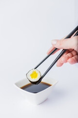 Female dipping tasty sushi makaki or uramaki with chopsticks into bowl with soy sauce on white background. Space for copy.