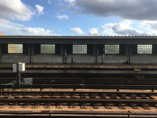 Empty overground subway platform with subway tracks in foreground. Blue sky and puffy clouds at vacant New York City train station, empty city, decline in public transport due to Corona Virus.