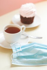 Cup of coffee and disposable face mask on a cafe table. Open restaurant, removal coronavirus COVID_19 restriction