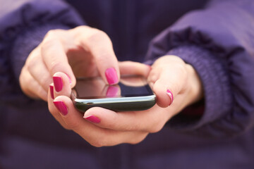 Young adult woman holding modern cellphone outdoors.