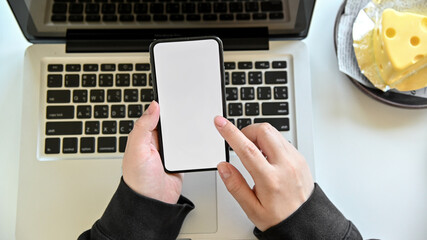 Top view woman using smart phone with laptop in office and hand holding smart phone empty screen.