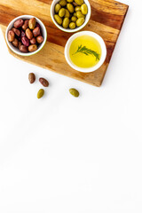 Olives and olive oil in bowls on cutting board on white top view copy space