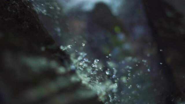 Close up view at a waterfall water droplets and spray flowing and splashing on rocks. Above waterfall angle. Outdoor, nature concept.