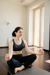 Fototapeta premium Home yoga. Young woman relaxing in her living room meditating on fitness mat. Leisure, self development, mental health and contemplation