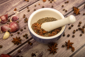 Allspice in a ceramic mortar and scattered garlic cloves, star anise and allspice on a wooden table. Close up.