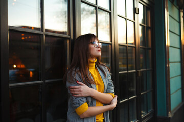 Beautiful dreamy girl in stylish sharp glasses. Near the shop window