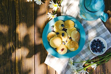 Mini pancakes with honeysuckle on a blue plate on a brown wooden background.