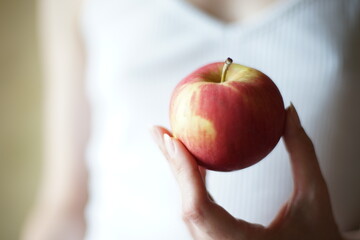 Red apple in female fingers on the background of a girl in a white shirt.