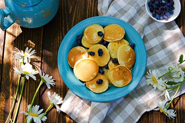 Mini pancakes with honeysuckle on a blue plate on a brown wooden background.
