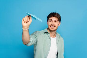 cheerful young man throwing paper plane on blue © LIGHTFIELD STUDIOS