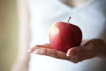 Red apple in female palm on the background of a girl in a white shirt