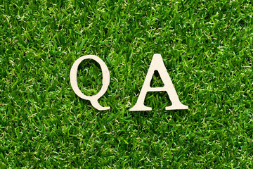 Wood alphabet letter in word QA (abbreviation of quality assurance or question and answer) on green grass background
