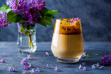 Summer still life with dalgona coffee in tall glass and lilac flowers on dark background. Instant...