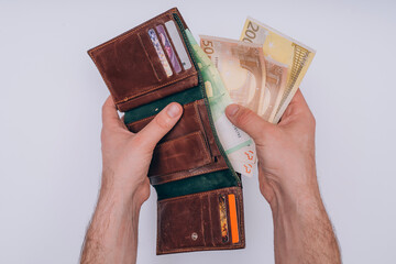man holds a wallet from which euro bills are visible on a white background
