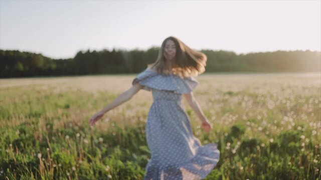 A caucasian beautiful wonan dancing on the beautiful field during summer sunseta. The woman wears beautiful dress and. The woman is smiling. Close up. SLOW MOTION