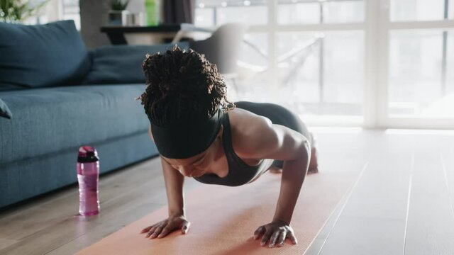 Black athletic young woman performing push-up exercises on mat practicing warm-up training bodybuilding at home. Keeping in shape. Fitness. Sports routine.