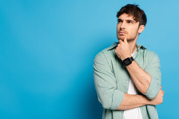 thoughtful young man looking away and touching chin on blue