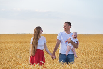 Young happy family resting in countryside. Mom dad and kid in wheat field