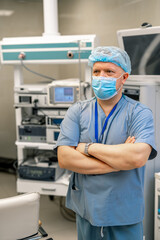 Naklejka premium Adult doctor standing cross hands in surgery room. Special modern equipment on the background.