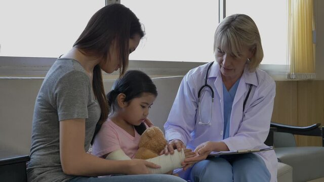 The female doctor in uniform was checking the girl's hand with her mother sitting on the side. Mother and daughter visit a doctor at the healthcare center.