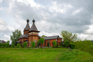 Fototapeta na wymiar Elegant wooden Church on a green meadow against a dark cloudy sky.