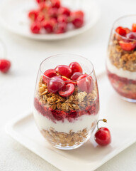 Granola Parfait with Yogurt, oat granola, fresh cherry, jam and honey in tall glass. Healthy dessert. Low depth of field, selective focus.