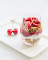 Granola Parfait with Yogurt, oat granola, fresh cherry, jam and honey in tall glass. Healthy dessert. Low depth of field, selective focus.