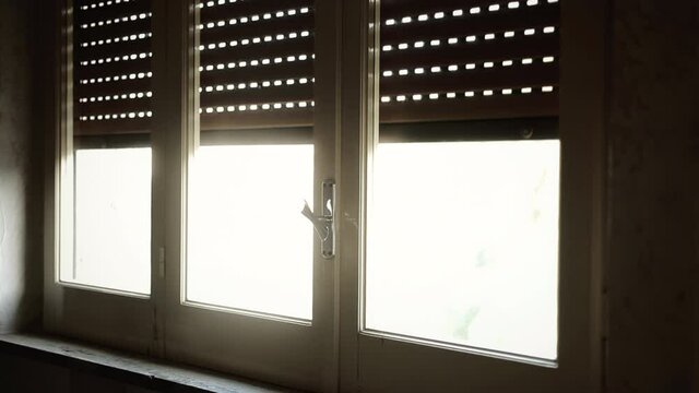 Angled shot: opening a rolling shutter (aka rollerblind), letting the sun rays come in the house.
