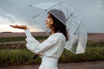 Young woman holding a clear, transparent umbrella on a stormy weather, checking the rain, on a dramatic dark blue sky background.
