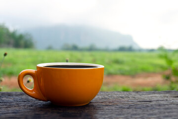 Black hot coffee drink on an old wooden table with a grass field and mountain nature landscape