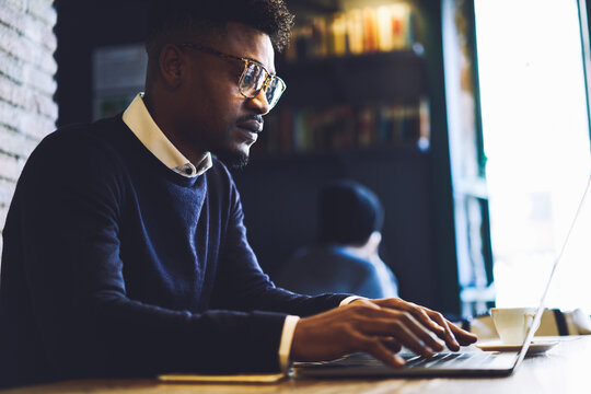 Skilled afro american copywriter creating text content for web advertising keyboarding on laptop computer connected to free wireless internet in coffee shop wifi zone working on free schedule