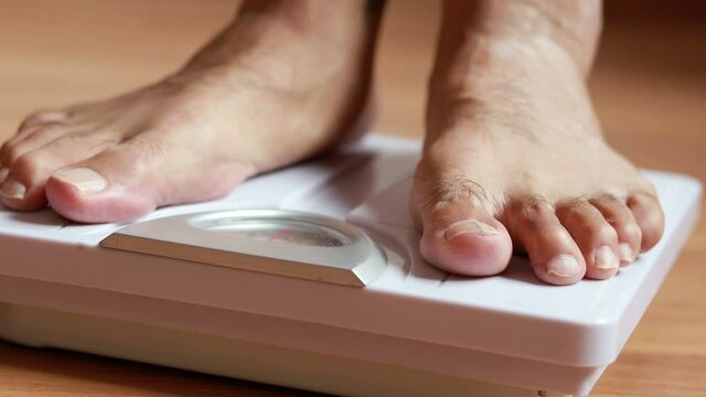 Close up man's feet standing on body weight scales for measure weight loss.Weighing scale to healthy slimming concept.