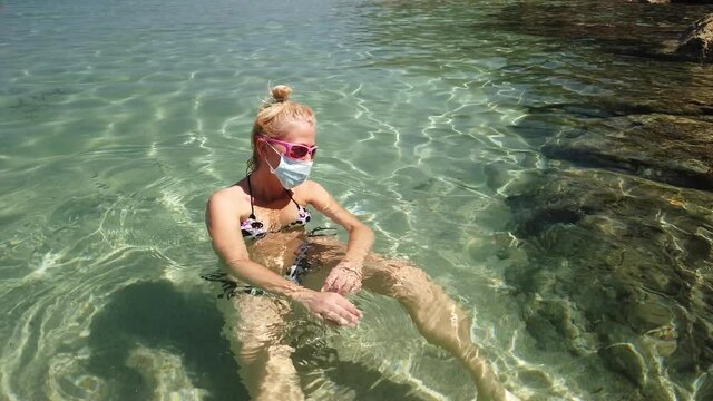Woman swimming in Fetovaia beach and crystal sea with a surgical mask during Covid-19. Blonde woman having a bath in Italian sea in Coronavirus quarantine. Holidays travel in COVID pandemic in Italy.