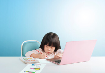 Smart little girl studying and drawing on table, isolated on blue background. Education concept learning.