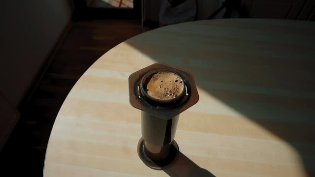 An downward view of an aeropress on a wooden table filled with coffee, waiting to be pressed