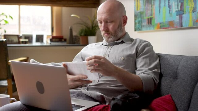 Pan up from a cute dog to a man looking through envelopes of bills stacking up