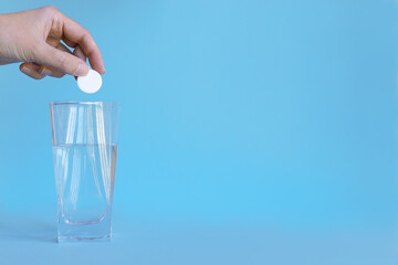 hand holds a white pill in his hands over a glass of water. Blue background.