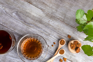 Healing beverage of birch mushroom chaga in glass cup and chaga pieces on diagonal wooden table. Top view, copy space.
