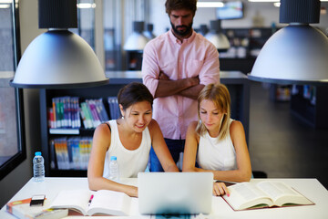 Group of international university students learning with books and laptop computer in library,...