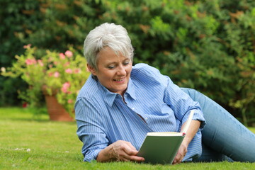 Attractive senior woman is reading a book in her leisure time in the garden in summer