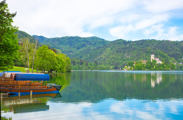 Fototapeta premium Traditional Pletna boat waiting for tourists on Lake Bled, with the lake island and charming little church in the background, famous tourists attraction in Slovenia