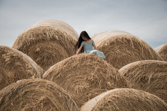Girl in blue dress sitting on stack of hay bales