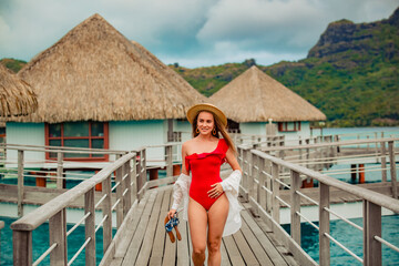beautiful girl in red swimsuit posing on dock near tropical houses on water