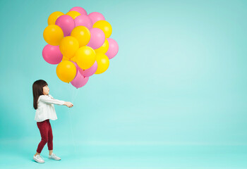 Fototapeta na wymiar Little girl holding helium balloons on plain background