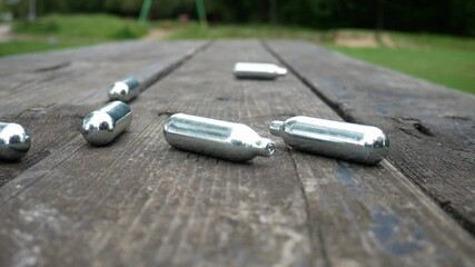 Multiple chrome drug nitrous oxide laughing gas drug cylinders pan left across wooden park bench
