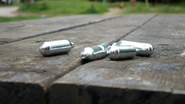 Used chrome nitrous oxide laughing gas drug cylinders dolly left across wooden park table